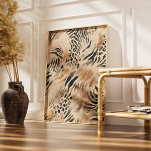 May include: A framed art print with a neutral animal print design. The artwork features a mix of zebra and leopard patterns in shades of beige, brown, and black. The print is displayed in a light-colored wooden frame, leaning against a white wall.