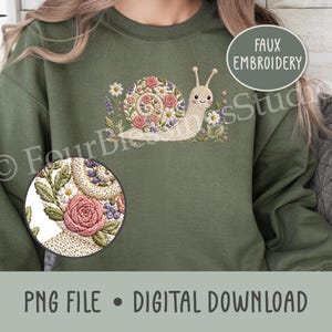 May include: An olive green sweatshirt featuring a faux embroidery design of a snail with a shell made of pink roses, white daisies, and purple flowers. A circular inset shows a magnified view of the floral snail shell texture and detail.