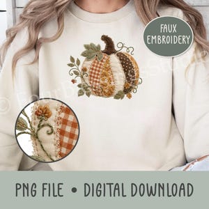 May include: A cream-coloured sweatshirt featuring a central faux embroidery design of a pumpkin composed of various patterned fabric segments in orange, brown, and white. The pumpkin is accented with green leaves and vines. Text reads FAUX EMBROIDERY.