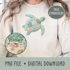 May include: A cream-colored sweatshirt featuring a faux embroidery design of a sea turtle. The turtle is composed of various light blue, teal, and beige patterned fabric patches, including polka dots, gingham, and floral prints with visible stitching.