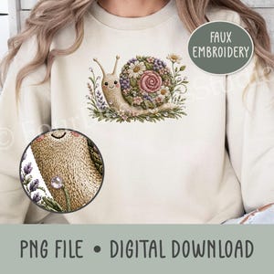 May include: A beige sweatshirt featuring a faux embroidery graphic of a smiling snail with a shell made of colorful flowers and greenery. A circular inset shows a magnified view of the snail's textured body and a small purple crystal accent.