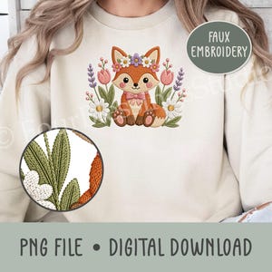 May include: A cream-colored sweatshirt featuring a central faux embroidery design of a seated orange fox wearing a pink bow, surrounded by colorful flowers including tulips and daisies. A circular inset shows a magnified view of the green leaves.