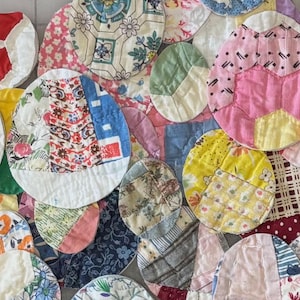 May include: A collection of colorful, quilted fabric circles and ovals in various sizes. The patchwork pieces feature floral, geometric, and patterned designs in shades of pink, blue, yellow, and red. The pieces are arranged on a grid.