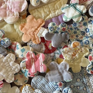 May include: A collection of handmade fabric flower appliqués in various colors and patterns. The flowers are made from quilted fabric and feature a variety of floral and striped designs. The color palette includes pinks, reds, blues, and yellows.