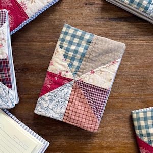 May include: Several rectangular notebooks featuring quilted fabric covers with patchwork designs. The covers display various patterns including blue and white gingham, red plaid, floral prints, and beige textures, all stitched together in triangular segments.