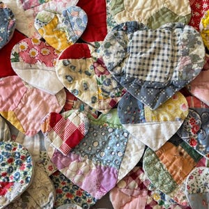 May include: A collection of handmade heart-shaped fabric patches in various colors and patterns. The patchwork hearts feature floral, gingham, and solid fabrics, creating a vintage, handcrafted aesthetic. The hearts are arranged closely together.