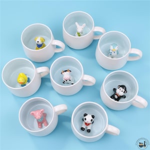 Pode incluir: Um conjunto de canecas de cerâmica branca, cada uma com uma figura de animal diferente no interior. Os animais incluem um cão, um coelho, um pato, uma vaca, um pinguim, um macaco, um porco e um panda. As canecas têm um design simples.