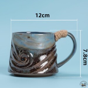 May include: A ceramic mug with a blue and dark brown swirled glaze, featuring a textured spiral pattern on the body and a handle wrapped in tan rope. The mug measures 12 cm in width and 7.8 cm in height as indicated by the visible measurement lines.