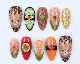 May include: A collection of ten uniquely designed nail art pieces. The designs include sushi, a bear, and other food-themed decorations. The nails are painted in various colors, including brown, green, red, and gold, with intricate details.
