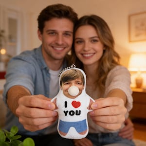 Puede incluir: Muñeco de peluche personalizado con la foto de una cara y una nariz de chicle. El muñeco lleva una camiseta blanca con las palabras "I ❤️ YOU" y pantalones cortos azules. Tiene un llavero.