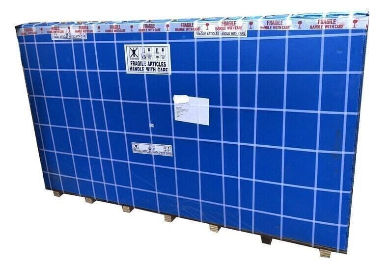 May include: Large, rectangular package wrapped in blue plastic with a grid pattern. White tape with "FRAGILE ARTICLES HANDLE WITH CARE" is visible. The package rests on wooden supports and has shipping labels.