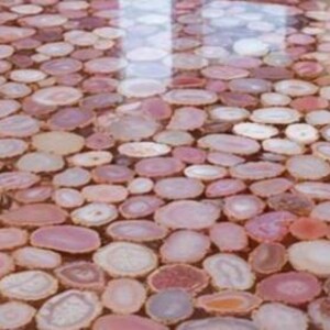 May include: A close-up view of a surface covered in polished, oval-shaped agate slices. The slices vary in shades of pink, beige, and white, creating a mosaic-like pattern. The surface reflects light, suggesting a glossy finish. The overall effect is decorative and natural.