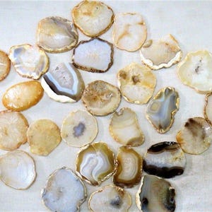 May include: A collection of agate slices in various shapes and sizes. The slices display a range of colors, including beige, brown, and white, with unique patterns and crystal formations. These decorative stones are ideal for crafts or home decor.