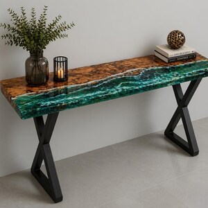 Puede incluir: Una consola moderna con un diseño único. La encimera presenta un diseño de resina epoxi marrón y verde que se asemeja a una costa. Tiene patas de metal negro y está decorada con un jarrón, un candelabro y una esfera decorativa.