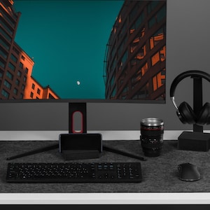May include: A contemporary computer setup with a black desktop tower, monitor showing a cityscape, keyboard, mouse, headphones, and a thermal cup. The setup is on a white desk with a grey felt mat.