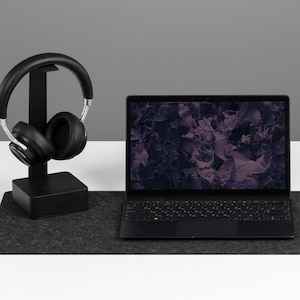 May include: A black laptop, mouse, and headphones sit on a dark grey felt desk mat. The laptop screen shows a dark floral pattern. The headphones are on a black stand.