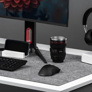 Puede incluir: Una configuración de computadora moderna con una torre de computadora de escritorio negra, un monitor que muestra una flor roja, un teclado, un ratón, auriculares y una taza de café. La configuración está sobre un escritorio blanco con una alfombrilla de fieltro gris.
