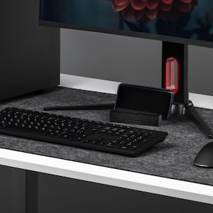 May include: A contemporary computer setup with a black PC tower, monitor showing a red flower, keyboard, mouse, and headphones. The setup is on a white desk with a grey felt mat.