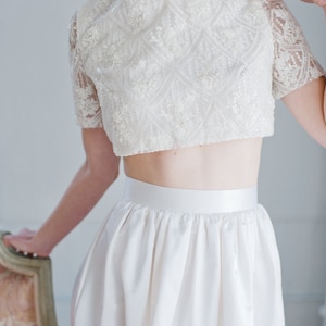 May include: A white crop top with a delicate lace design and a matching white skirt. The top has a round neckline and short sleeves.