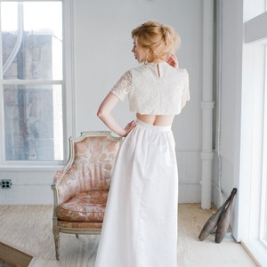 May include: A white lace crop top with a white skirt. The skirt is long and flowing, and the top has a fitted bodice and short sleeves.