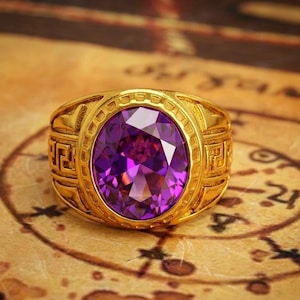Puede incluir: Un anillo dorado con una gran gema púrpura de forma ovalada. El anillo tiene un diseño detallado alrededor de la gema y en la banda. El anillo está sobre un fondo de estilo vintage con marcas descoloridas.