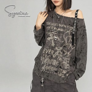 Puede incluir: Una camiseta gris desgastada de manga larga con un diseño asimétrico. La camiseta presenta texto gráfico y un detalle de correa negra. El texto incluye las palabras "EVER", "Reforme", "Artistique" y "STAR GIRL".