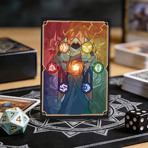 Puede incluir: Una funda para cartas con un diseño de vidriera que representa una figura central y símbolos en rojo, naranja, amarillo, verde, azul y morado. La funda tiene un borde negro y está sobre una alfombrilla negra con un patrón de estrellas blancas. También se ven dados y cartas.