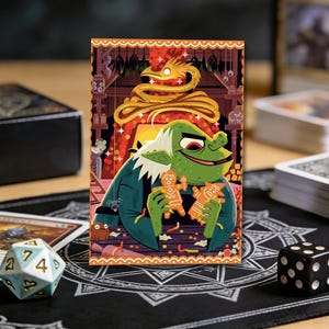 May include: A colorful illustration of a green goblin holding two gingerbread men. The goblin has white hair and is wearing a blue coat. A golden serpent and a decorative border frame the image. Dice and playing cards are in the background.