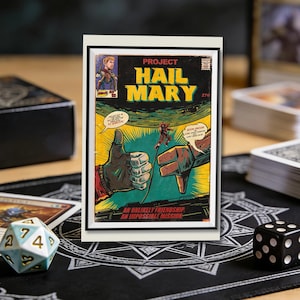 Può includere: Una copertina di fumetto incorniciata con il titolo "HAIL MARY" in giallo e bianco. L'opera presenta un gesto della mano con il pollice in su e il pollice in giù, con una figura al centro. Il testo "AN UNLIKELY FRIENDSHIP, AN IMPOSSIBLE MISSION" è in basso.