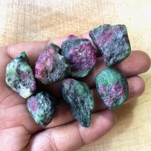 Peut inclure: Une collection de pierres brutes de rubis et de zoïsite. Les pierres présentent un mélange de couleurs, notamment du rouge profond, du vert et du noir. Les pierres précieuses sont tenues dans une main, mettant en valeur leur état naturel et non poli.