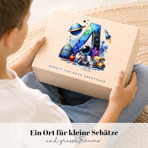 Peut inclure: Un coffret en bois avec un design color&eacute; sur le th&egrave;me de l'espace. Le motif comprend une grande lettre "A" remplie d'un motif de galaxie, une plan&egrave;te, une fus&eacute;e et un astronaute. Le coffret porte l'inscription "BEREIT F&Uuml;R NEUE ABENTEUER" et "Anton".