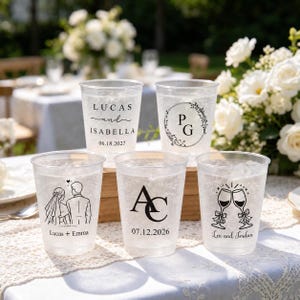 May include: Five clear plastic cups featuring black printed designs. One shows Lucas and Isabella with a date, one has initials PG in a wreath, one depicts a couple with Lucas + Emma, one shows initials AC with a date, and one displays two glasses with Lee and Jordan.