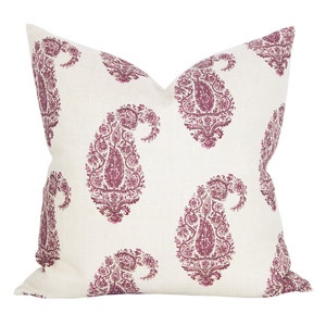 May include: A square decorative pillow with a white background and a repeating pattern of large, ornate paisley designs in a deep magenta color. The pillow has a soft, textured appearance.