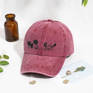 Op de afbeelding: Bordeauxrode baseballcap met geborduurde afbeeldingen van Mickey en Minnie Mouse. De cap heeft een gebogen klep en een distressed, vintage look. De cap is een klassiek zes-panelen ontwerp.