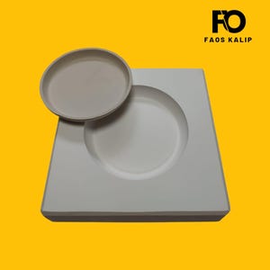 Pode incluir: Um molde de cerâmica branco com uma reentrância circular e um prato pequeno a condizer. O molde é retangular com cantos arredondados. O logótipo "FO FAOS KALIP" está no canto superior direito sobre um fundo amarelo.