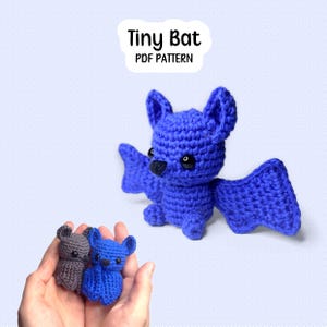 Può includere: Un pipistrello amigurumi all'uncinetto in blu brillante con occhi di sicurezza neri e un piccolo naso nero. Il testo Tiny Bat PDF PATTERN è visualizzato sopra. Un pipistrello grigio e uno blu sono tenuti in mano per mostrare la scala.