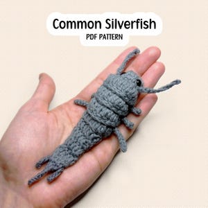 May include: A grey crocheted silverfish insect with segmented body parts, thin antennae, and small legs. The text above the object reads Common Silverfish PDF PATTERN. The item is crafted from yarn with a visible textured stitch pattern.