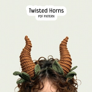 May include: A crochet accessory featuring two large, spiraled, brown horns and small green leaves at the base. The text "Twisted Horns PDF PATTERN" is displayed above the horns. The design is crafted with visible yarn stitches and textures.