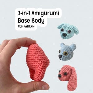May include: A coral-colored, crocheted amigurumi base body is held in a hand, with three crocheted dog heads in the background. The dog heads are light blue, light gray, and pink. Text reads "3-in-1 Amigurumi Base Body PDF Pattern."