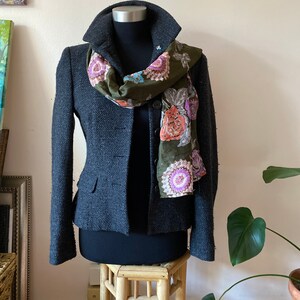 May include: A charcoal gray blazer with a floral patterned scarf. The blazer has a collar and two buttons. The scarf is green, pink, and purple.