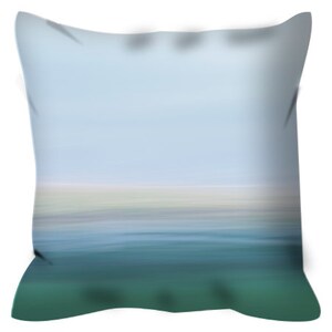 Op de afbeelding: Een decoratief kussen met een wazig abstract ontwerp van een blauwe lucht en groen water. Het kussen heeft een groene rand.