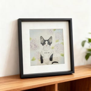 May include: A framed art print showing a black and white cat wearing a sweater with the words "cute cat." The background features soft purple flowers. The frame is black.