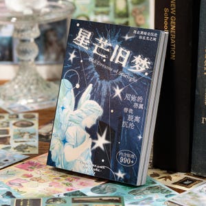 May include: A decorative sticker book with a celestial theme. The cover features an illustration of an angel, stars, and the text "Old Dreams of Starlight" in English and Chinese characters. The book is surrounded by other stickers.