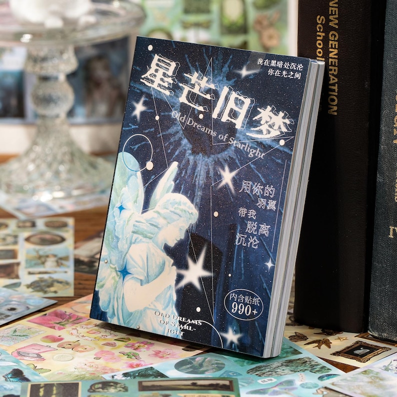 May include: A decorative sticker book with a celestial theme. The cover features an illustration of an angel, stars, and the text "Old Dreams of Starlight" in English and Chinese characters. The book is surrounded by other stickers.