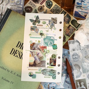 May include: A collage of stickers and ephemera on a white paper, featuring a butterfly, floral elements, and text like "Escape the ordinary" and "Keep smiling life is beautiful." The scene includes a book and other decorative stickers.