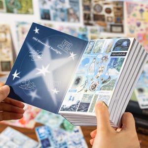 May include: A stack of decorative stickers with a blue cover featuring the text "Old Dreams of Starlight" and star illustrations. The stickers inside showcase various artistic designs in shades of blue and white, with a dreamy aesthetic.