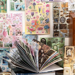 May include: A collection of decorative stickers and a journal. The stickers feature floral designs, butterflies, and other nature-inspired elements. The journal is open, displaying various sticker sheets with diverse illustrations and colors.