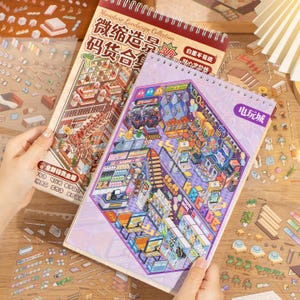 Op de afbeelding: Twee spiraalgebonden notitieboekjes met gedetailleerde illustraties. Eén toont een supermarkt, de andere een arcadehal. De notitieboekjes maken deel uit van de Miniature Landscape Collection, met tekst in het Chinees.
