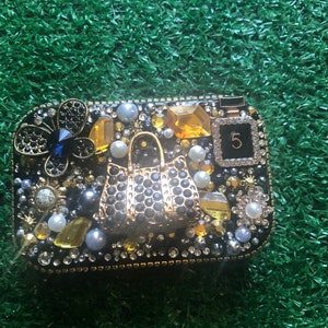 May include: A black and gold jeweled trinket box with a small purse design and the number "5" on the side.