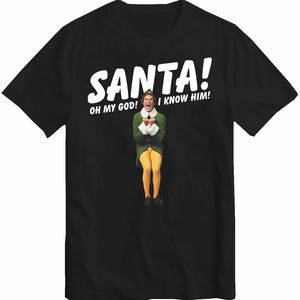 Puede incluir: Camiseta negra con una imagen de la película Elf. El texto blanco dice "SANTA! OH MY GOD! I KNOW HIM!" encima de una imagen de Buddy el Elfo con su disfraz. La imagen es un plano de cuerpo entero de Buddy.